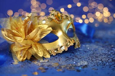 Photo of Beautiful carnival mask on blue glitter background against blurred lights, closeup. Bokeh effect