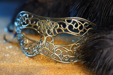 Photo of Beautiful carnival mask and black feathers on golden background, closeup