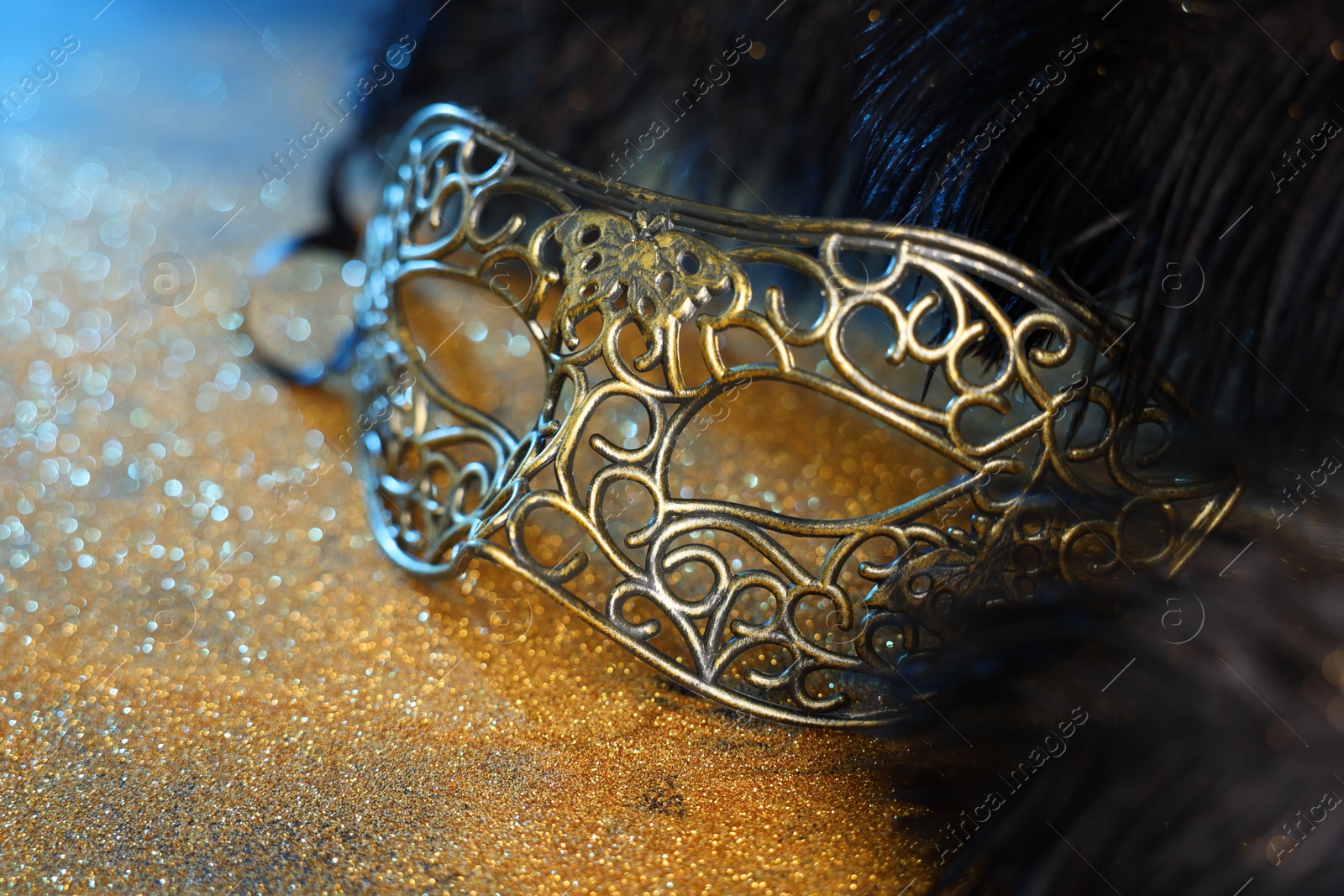 Photo of Beautiful carnival mask and black feathers on golden background, closeup