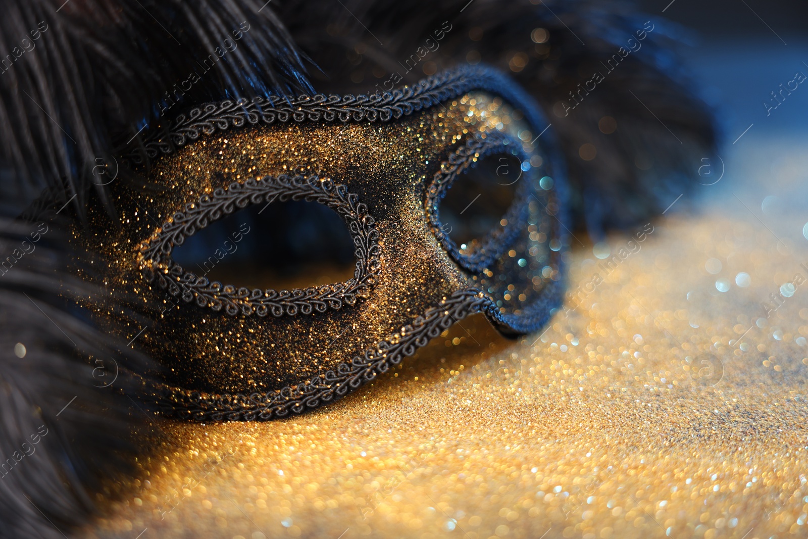 Photo of Beautiful carnival mask and black feathers on glitter background, closeup