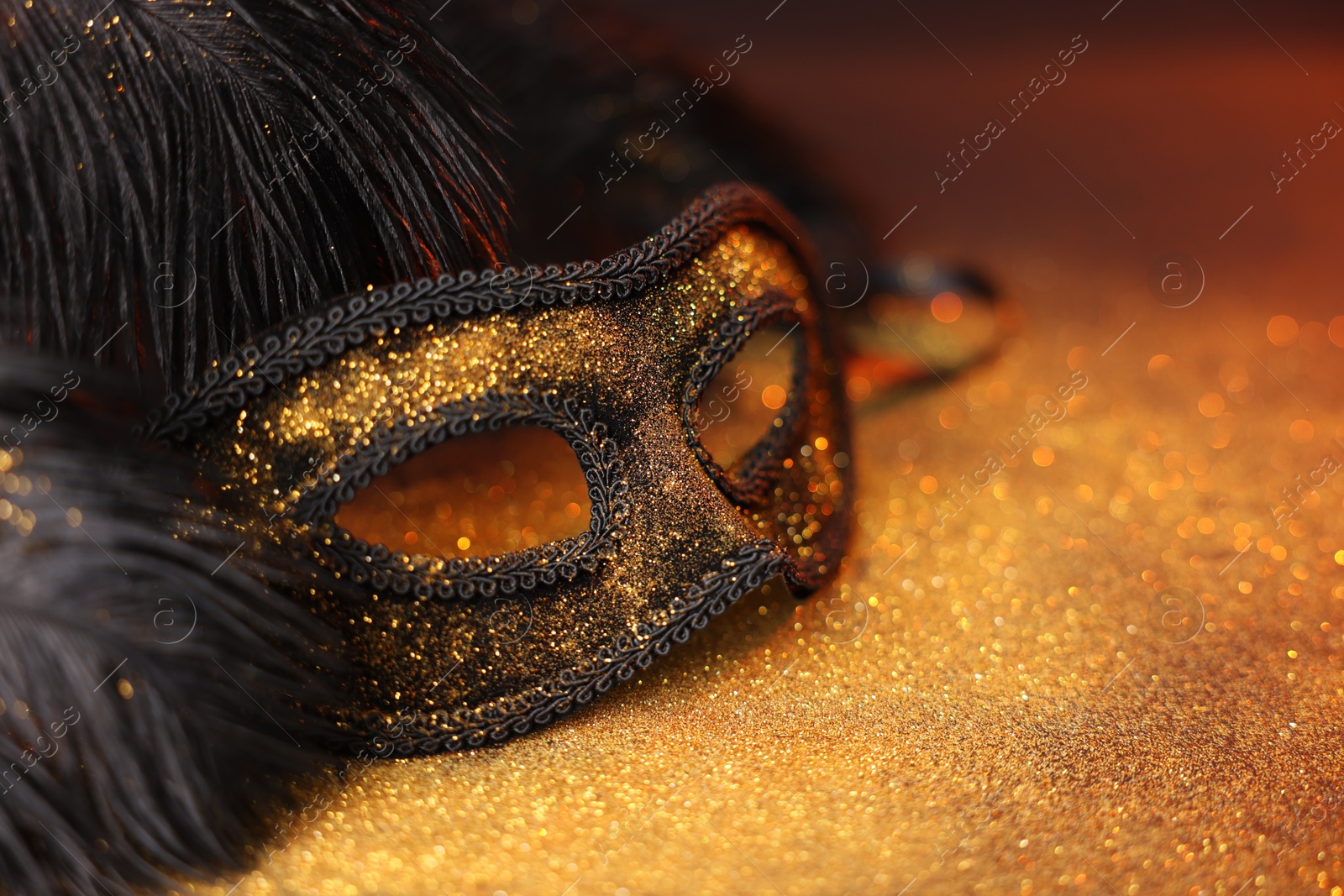 Photo of Beautiful carnival mask and black feathers on glitter background, closeup. Space for text