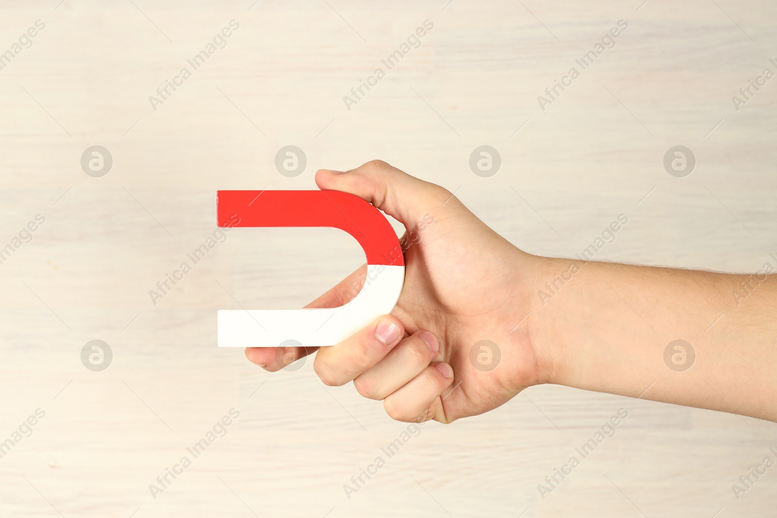 Photo of Man holding horseshoe magnet against white wooden background, closeup