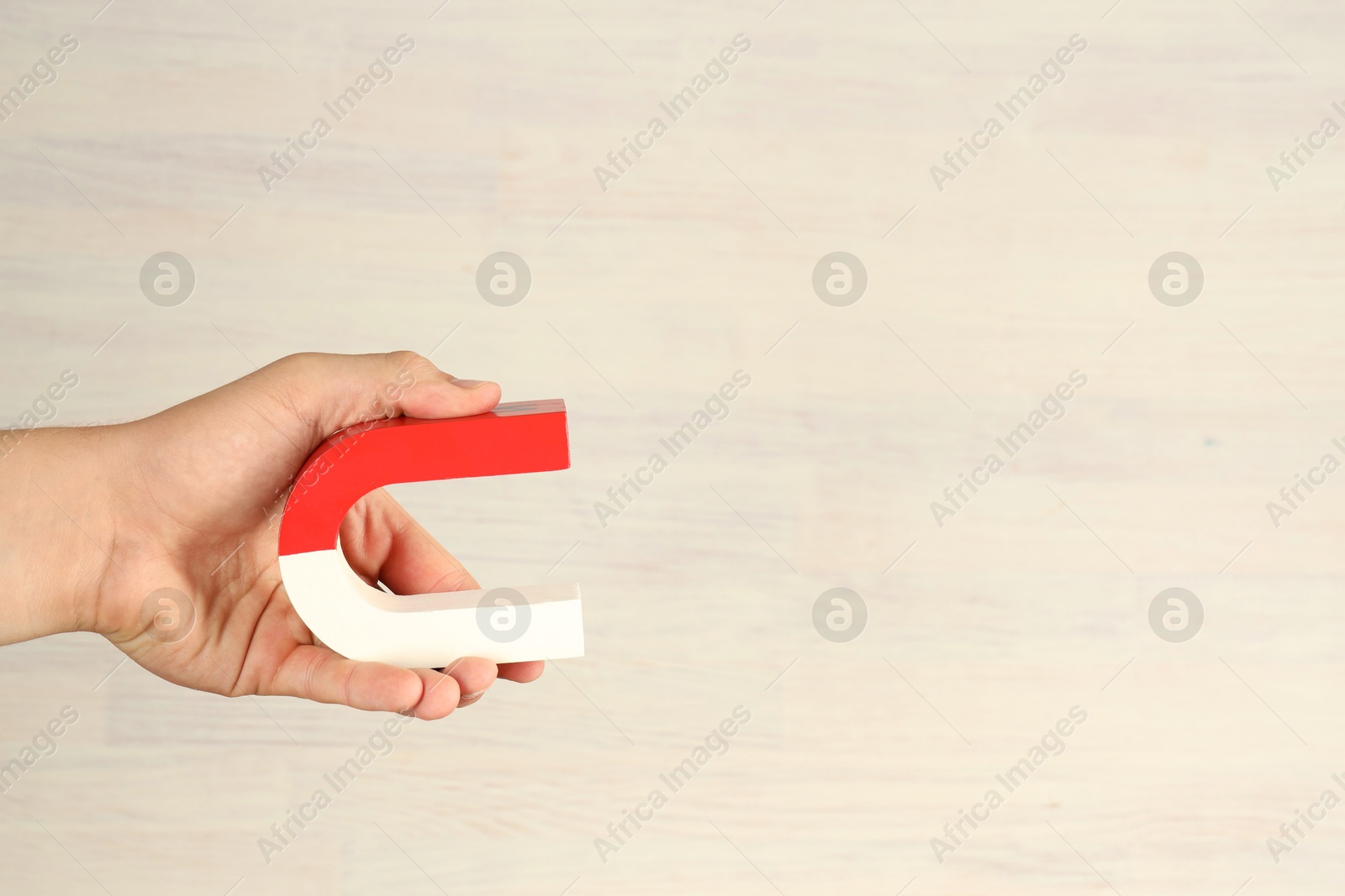 Photo of Man holding horseshoe magnet against white wooden background, closeup. Space for text