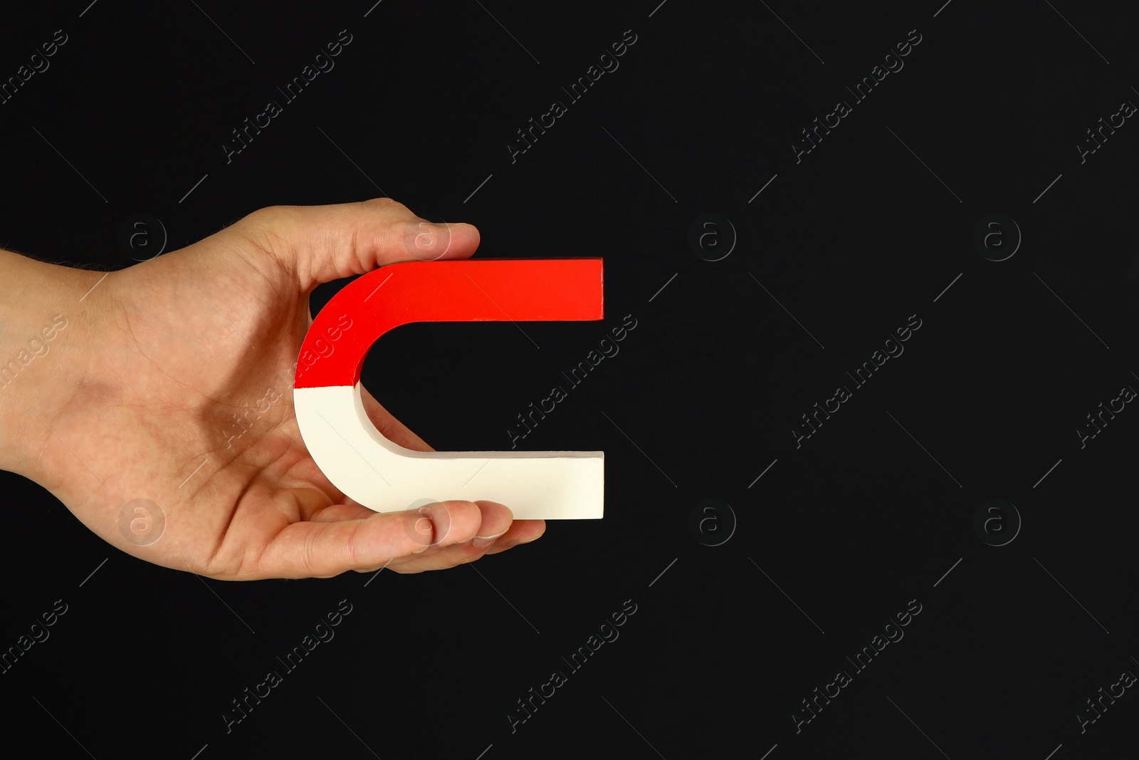 Photo of Man holding horseshoe magnet on dark background, closeup. Space for text