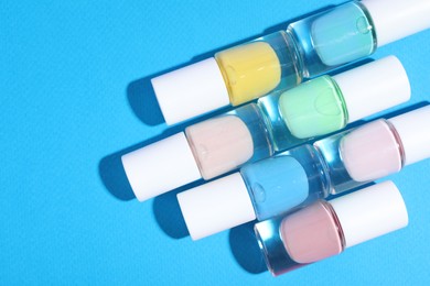 Photo of Nail polishes in bottles on light blue background, flat lay. Space for text