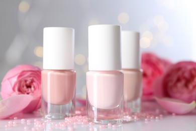 Photo of Nail polishes in bottles, beads and beautiful flowers on white table, closeup