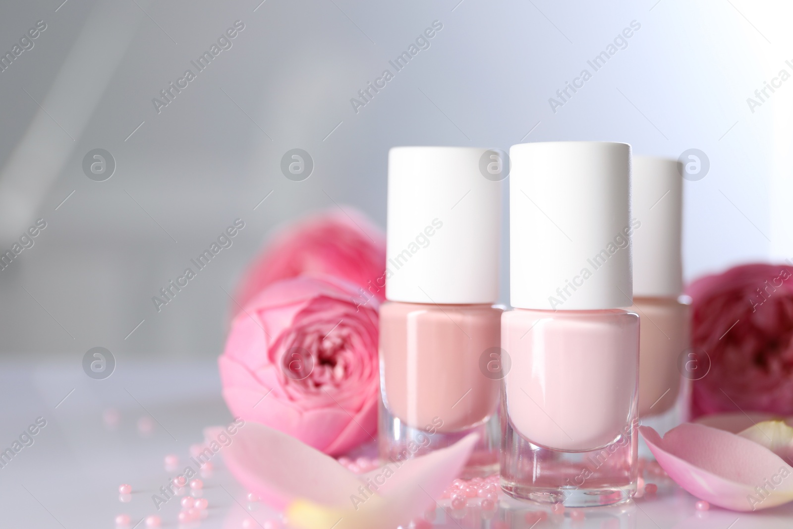 Photo of Nail polishes in bottles, beads and beautiful flowers on white table, closeup. Space for text