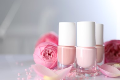 Photo of Nail polishes in bottles, beads and beautiful flowers on white table, closeup. Space for text