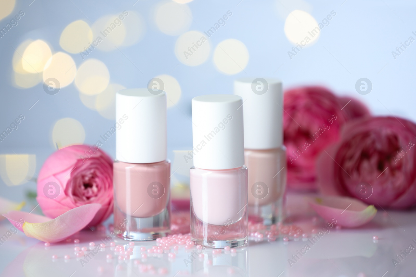 Photo of Nail polishes in bottles, beads and beautiful flowers on white table, closeup