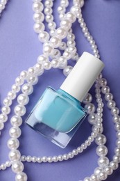 Photo of Nail polish in bottle and necklace on purple background, flat lay