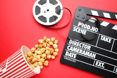 Photo of Movie clapper, sweet popcorn and film reel on red background, flat lay