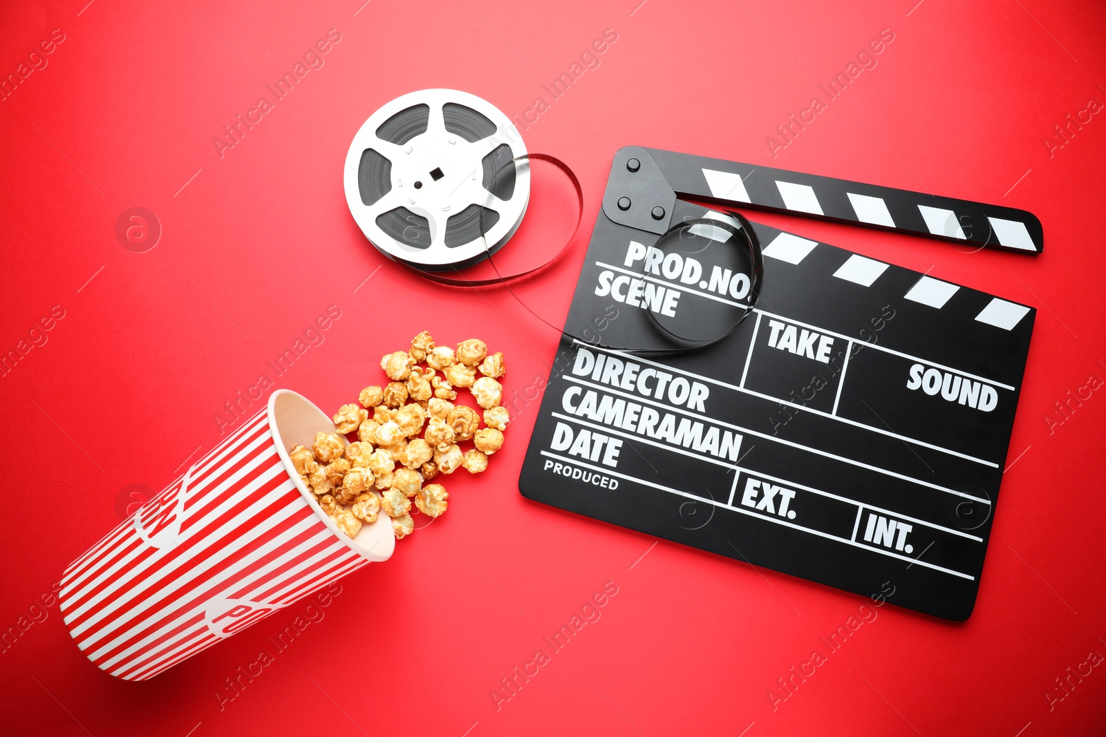 Photo of Movie clapper, sweet popcorn and film reel on red background, flat lay