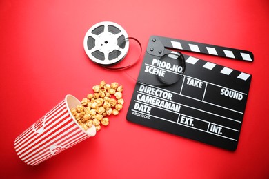 Photo of Movie clapper, sweet popcorn and film reel on red background, flat lay