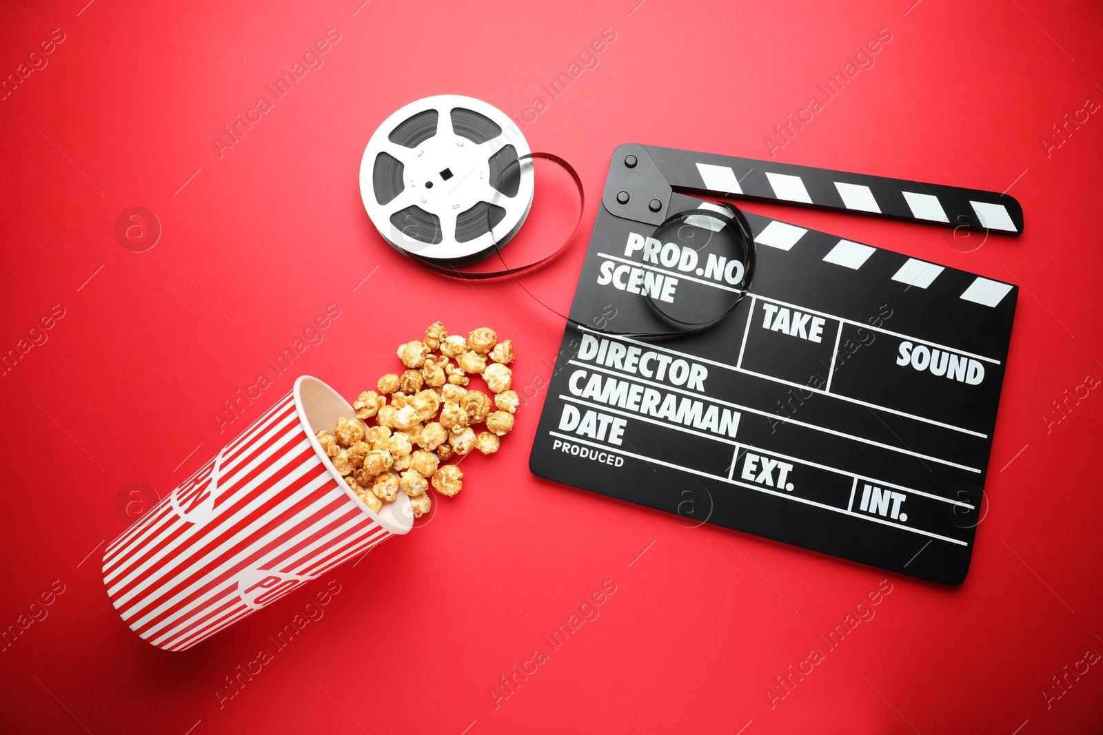 Photo of Movie clapper, sweet popcorn and film reel on red background, flat lay