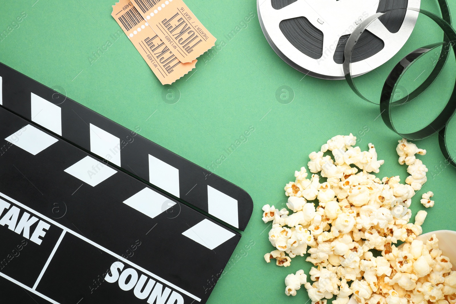 Photo of Movie clapper, tasty popcorn, tickets and film reel on green background, flat lay