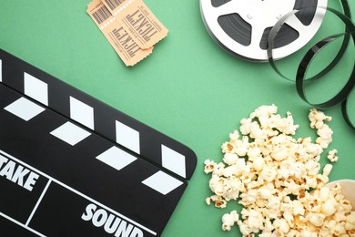 Photo of Movie clapper, tasty popcorn, tickets and film reel on green background, flat lay