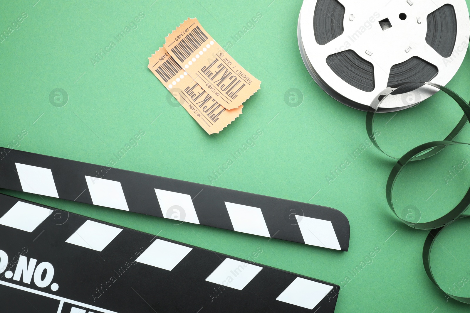 Photo of Movie clapper, tickets and film reel on green background, flat lay