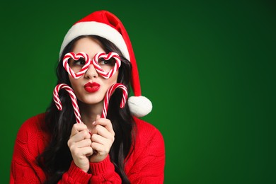 Photo of Beautiful woman in Santa hat and party glasses with candy canes on green background., space for text Christmas celebration