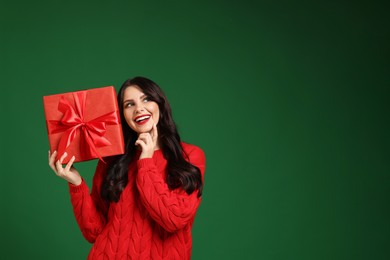 Beautiful woman with Christmas gift on green background, space for text