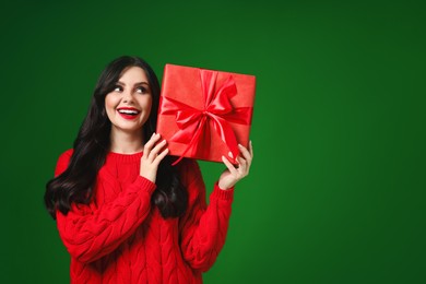 Photo of Beautiful woman with Christmas gift on green background, space for text