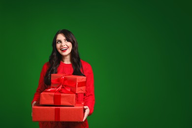 Beautiful woman with Christmas gifts on green background, space for text