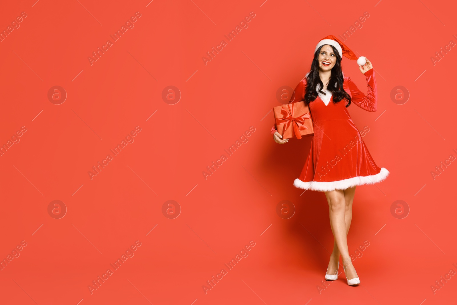 Photo of Beautiful woman in Mrs Claus costume with Christmas gift on red background