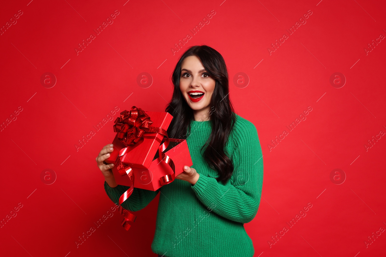 Photo of Beautiful woman opening Christmas gift on red background