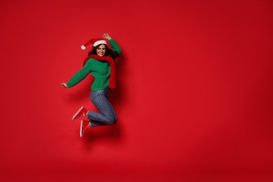 Photo of Happy woman in Santa hat jumping on red background. Christmas celebration