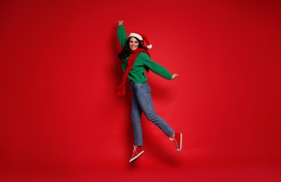 Photo of Happy woman in Santa hat jumping on red background. Christmas celebration