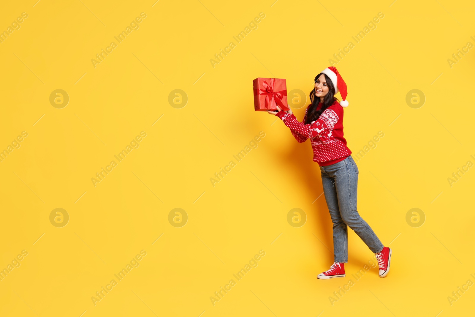 Photo of Woman in Santa hat with Christmas gift on yellow background, space for text