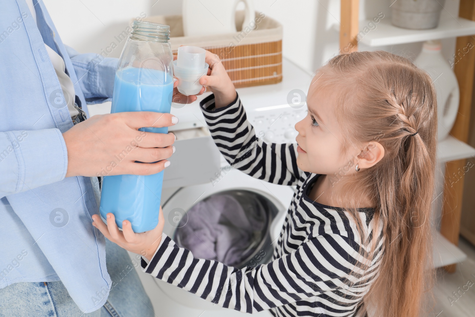 Photo of Little girl with detergent helping her mom doing laundry at home