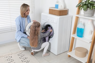 Photo of Little girl helping her mom doing laundry at home