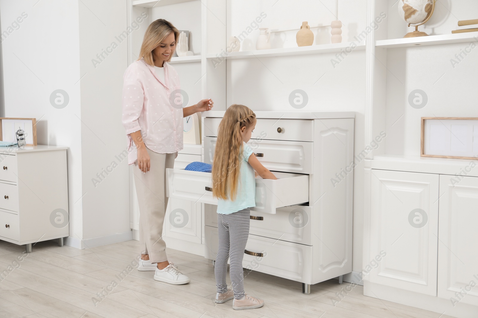 Photo of Little girl helping her mother putting clothes into drawers at home