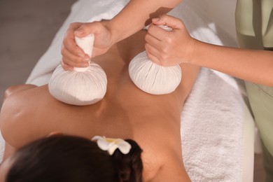 Photo of Woman receiving back massage with herbal bags in spa salon, closeup