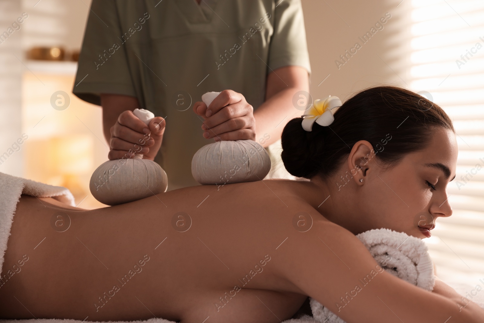 Photo of Woman receiving back massage with herbal bags in spa salon