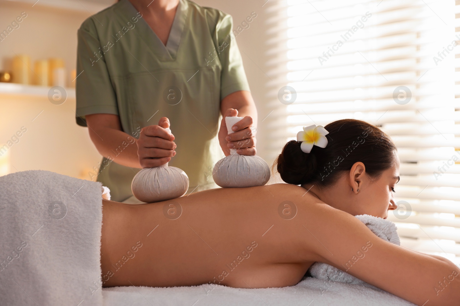 Photo of Woman receiving back massage with herbal bags in spa salon