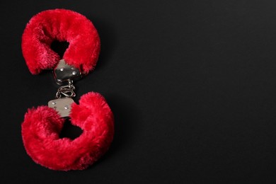 Photo of Bright fluffy handcuffs on black background, space for text