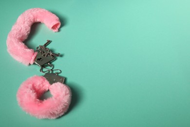 Photo of Bright fluffy handcuffs and keys on turquoise background. Space for text