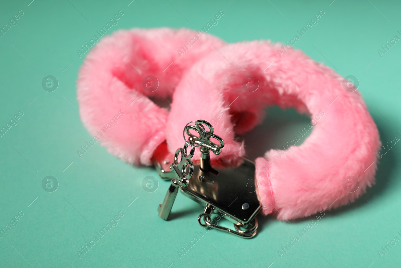 Photo of Bright fluffy handcuffs and keys on turquoise background, closeup