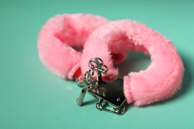 Photo of Bright fluffy handcuffs and keys on turquoise background, closeup