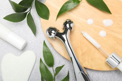 Photo of Metal face roller, gua sha tool, cosmetic products and green leaves on gray background, flat lay