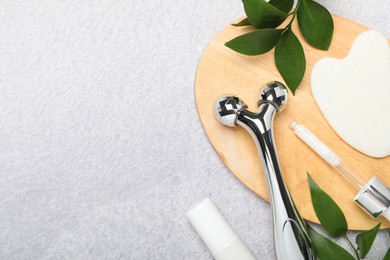 Photo of Metal face roller, gua sha tool, cosmetic products and green leaves on gray background, flat lay. Space for text