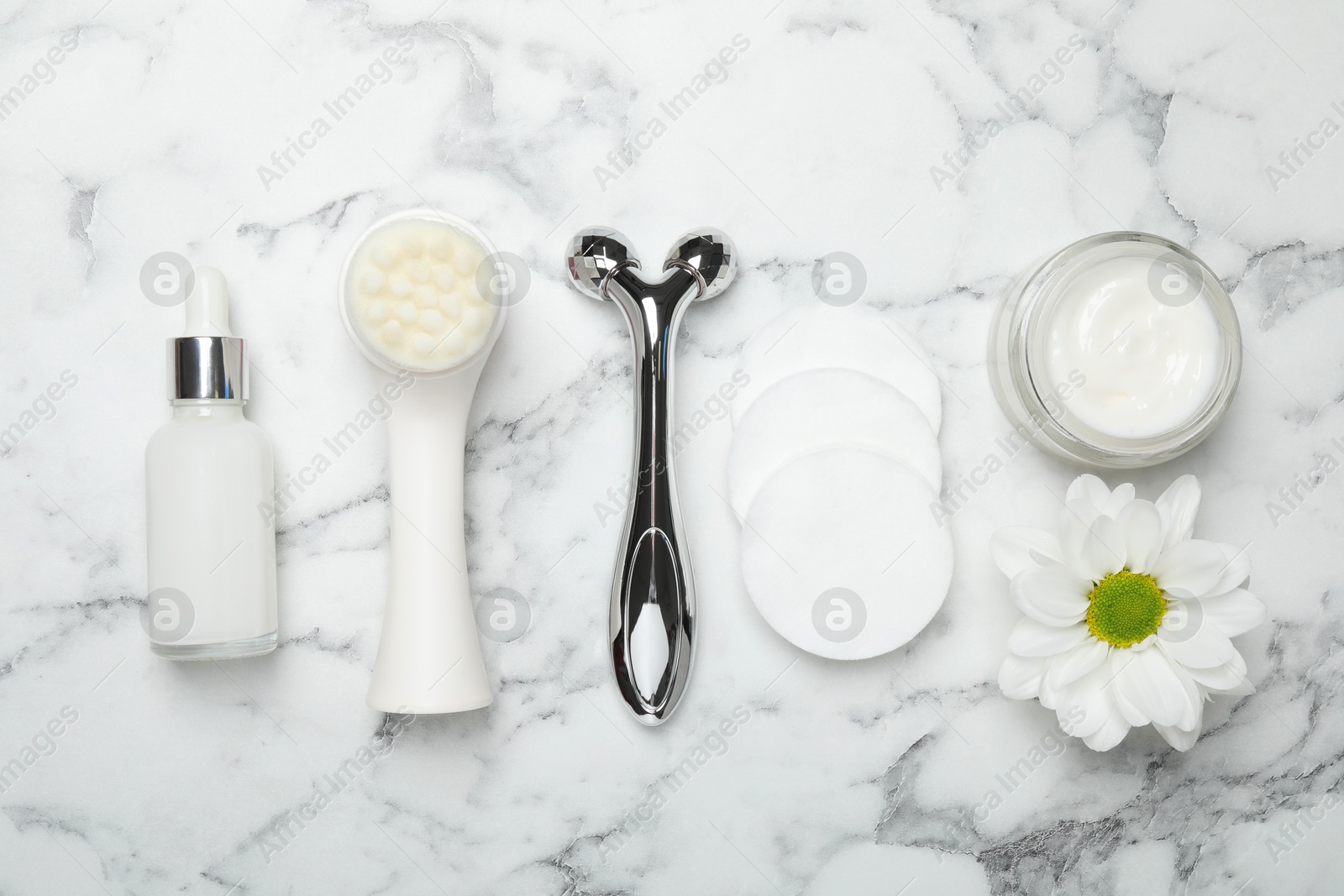 Photo of Metal face roller, cleansing brush, cosmetic products, cotton pads and chrysanthemum flower on white marble background, flat lay