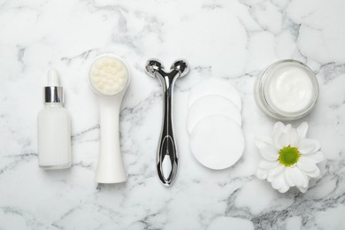 Photo of Metal face roller, cleansing brush, cosmetic products, cotton pads and chrysanthemum flower on white marble background, flat lay