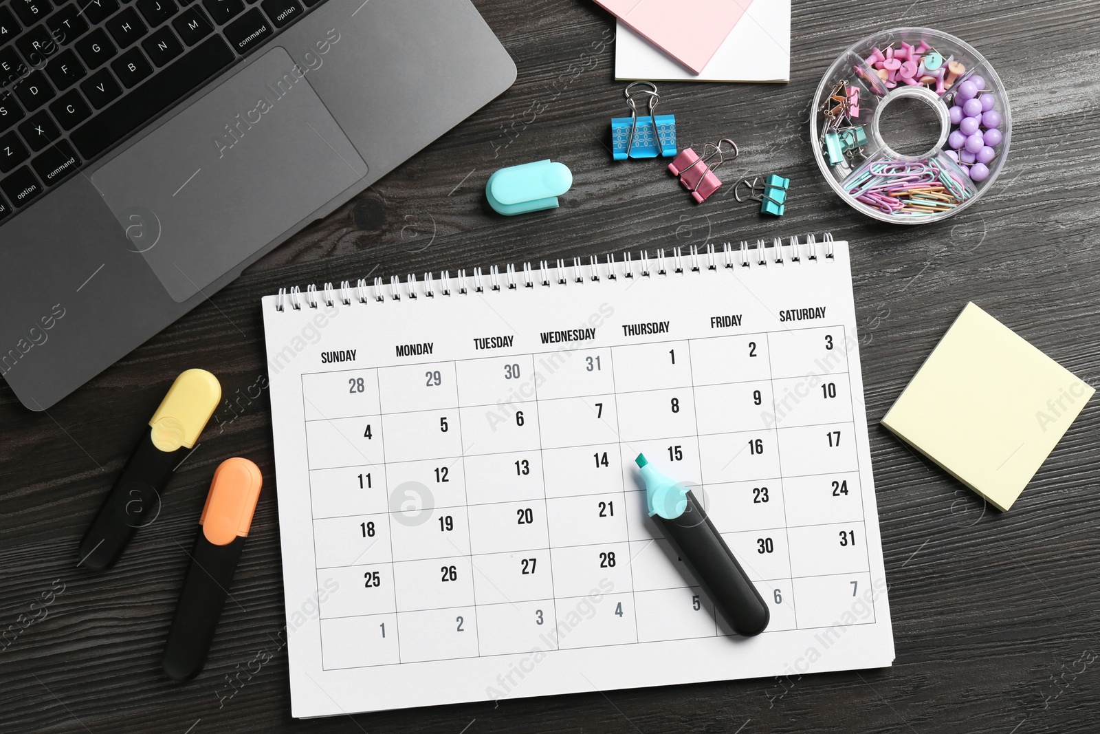 Photo of Timetable. Monthly planner, stationery and laptop on wooden table, flat lay