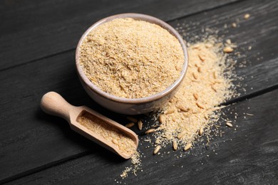 Photo of Oat bran in bowl, grains and scoop on black wooden table