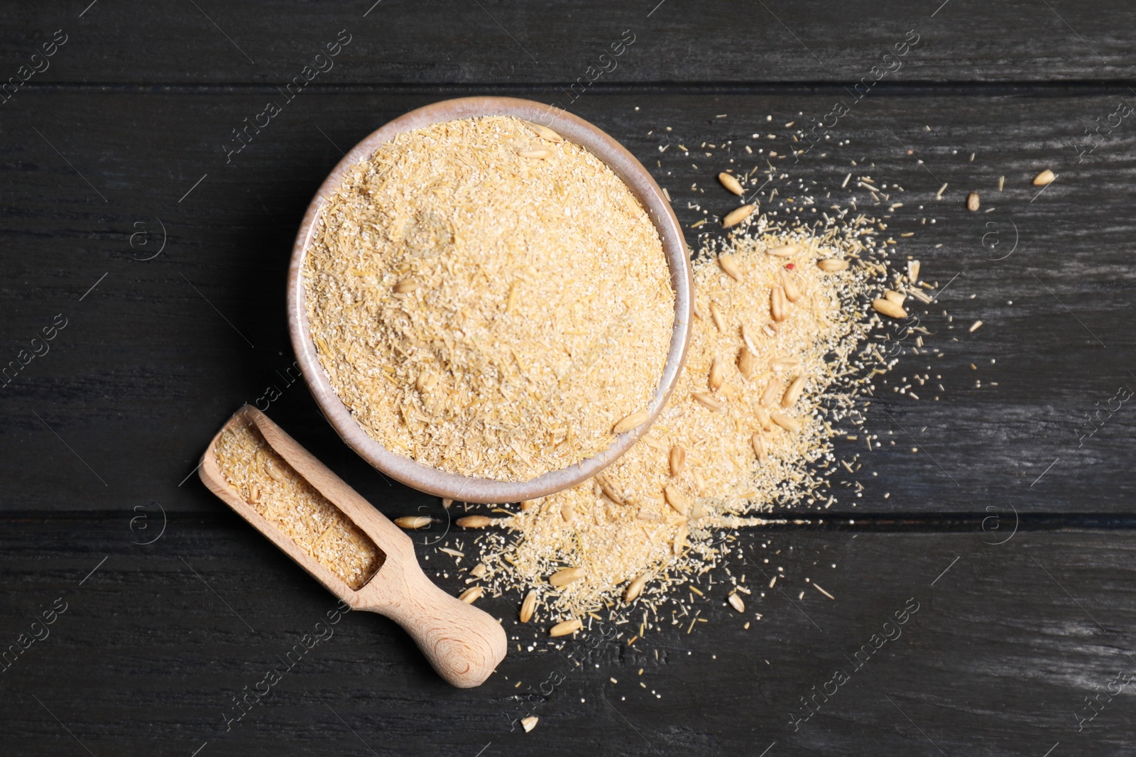 Photo of Oat bran in bowl, grains and scoop on black wooden table, top view