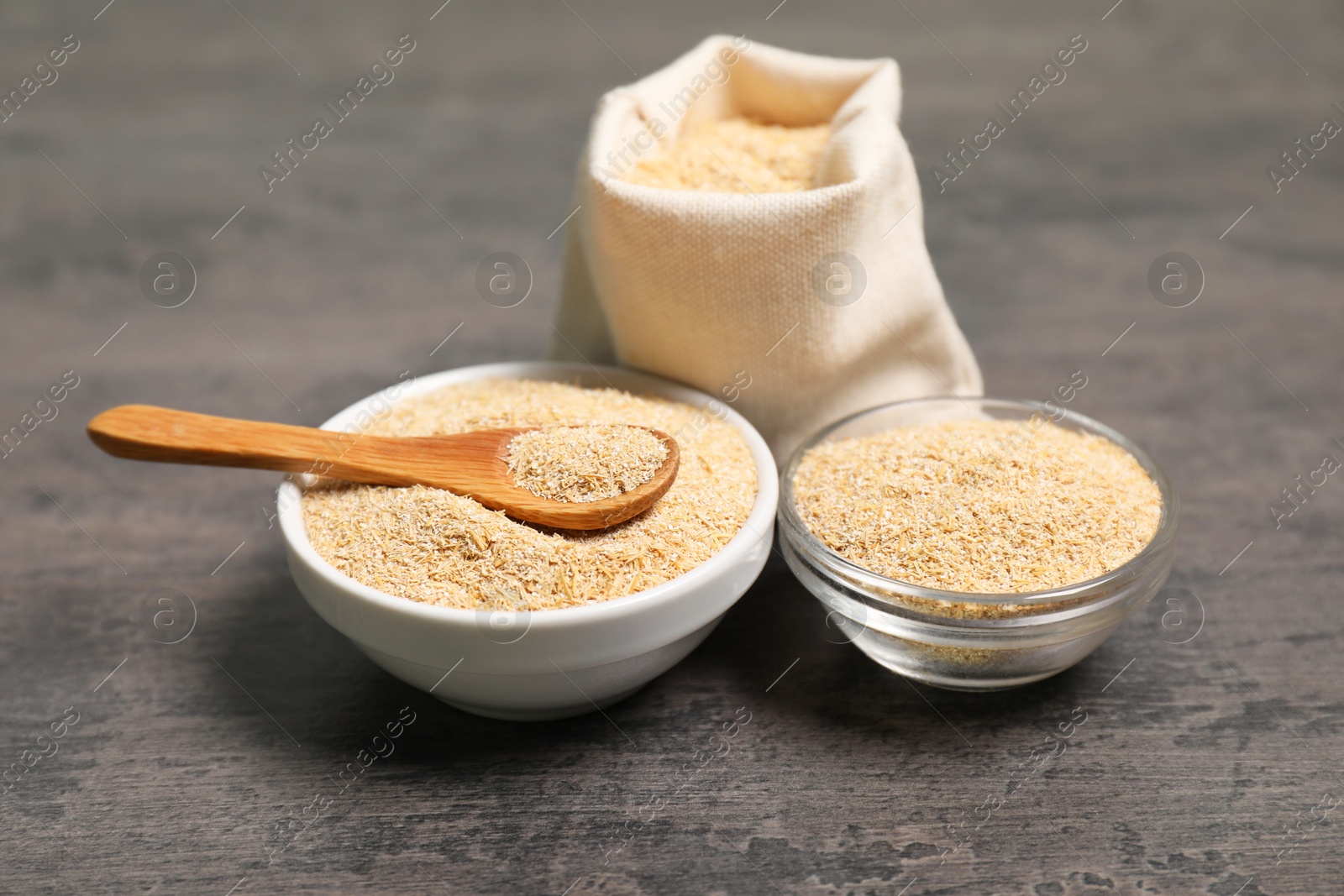 Photo of Oat bran in bowls, burlap bag and spoon on grey table, closeup