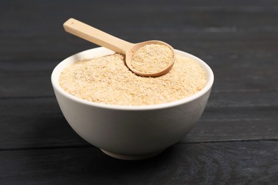 Photo of Oat bran in bowl and spoon on black wooden table, closeup