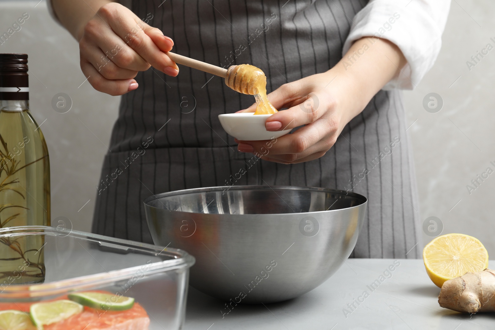 Photo of Woman adding honey at gray table, closeup